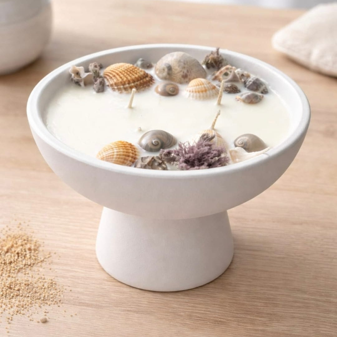 Seashell candle in a pedestal bowl by Velarte, featuring a decorative candle surrounded by seashells on a ceramic pedestal.