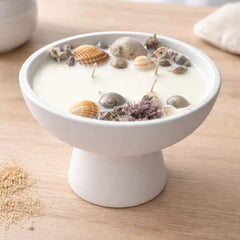 Seashell candle in a pedestal bowl by Velarte, featuring a decorative candle surrounded by seashells on a ceramic pedestal.