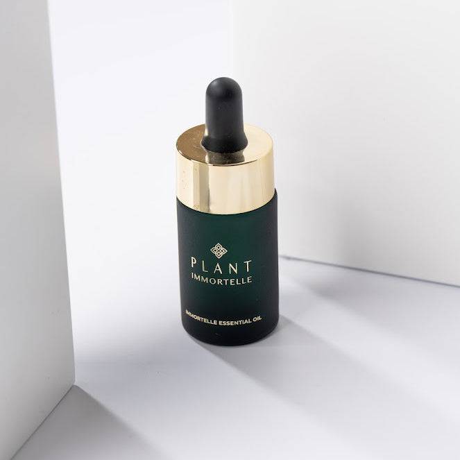 Small amber glass bottle of Plant Immortelle Essential Oil for skin care, labeled with brand name, on a neutral background.